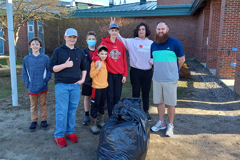 Students and teacher smiling in front of a big bag of trash they collected